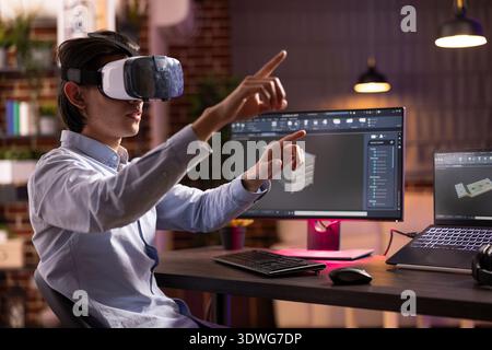 Asian male entrepreneur working from home, using vr glasses and computer aided design software for architectural products. Young man with virtual reality headset, modifying 3d prototype models. Stock Photo