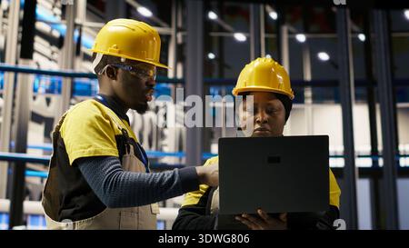 Engineering team doing brainstorming in smart factory, analyzing IoT sensor data. Industry 4.0 plant teamworking colleagues managing operational reliability of photovoltaic systems, camera B Stock Photo