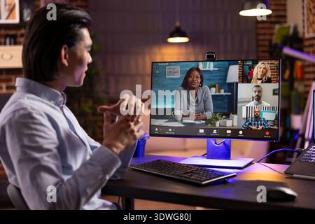 Focused asian man attending virtual business meeting from home office. Self employed guy sits confidently at desk, communicating with diverse online team and collaborating on remote work projects. Stock Photo