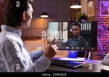 Self employed man and business partner join video call on desktop pc, discussing project details and collaborating online. Diverse male professionals communicate project planning from home office. Stock Photo