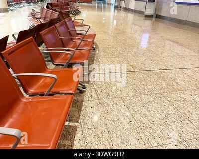 Red metal chairs are lined up in an airport waiting area, showcasing a polished granite floor with reflections and an empty space in the background Stock Photo