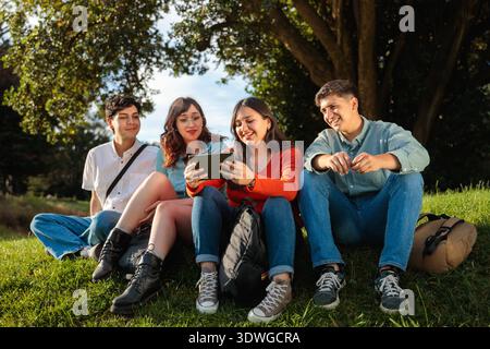 Group of students sitting on grass using tablet outdoors Stock Photo