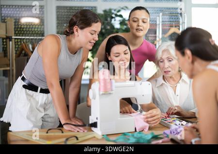 Young seamstress demonstrating stitching at machine to female students Stock Photo