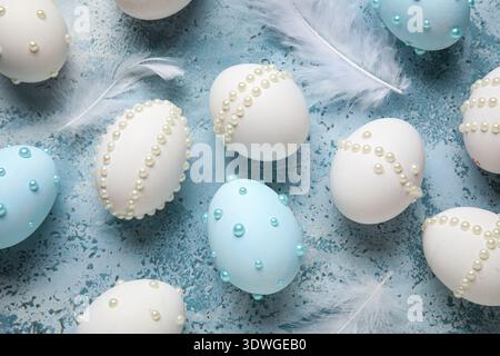Easter eggs decorated with pearls and feathers on blue grunge background, closeup Stock Photo