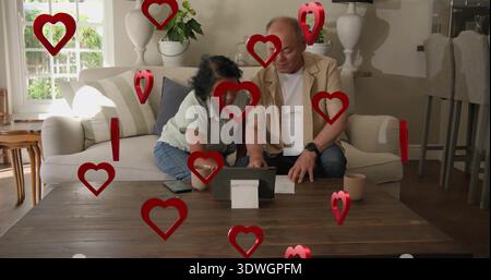 Reviewing couple in beige blazer and light blouse checking tablet on table at home, red hearts Stock Photo