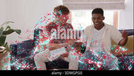 Holding envelope, men in brown, white shirts on sofa at home, other cheering amid confetti effect Stock Photo