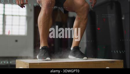 Jumping man landing feet on plyometric box in gym, wearing dark shorts, black shoes, chalk rising Stock Photo