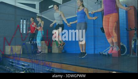 Jumping five adults in workout gear skipping ropes on raised platform in fitness studio with charts Stock Photo