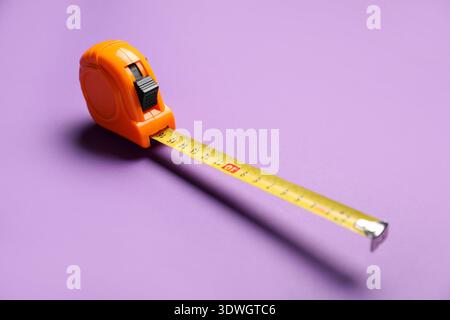 Orange measuring tape on violet background, closeup Stock Photo
