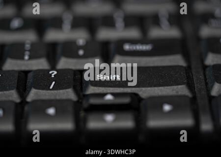 A close-up, high-angle macro photograph of a dusty black membrane keyboard featuring a shallow depth of field, highlighting the Shift, Enter, and ques Stock Photo