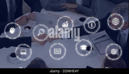 Shaking hands two business associates in suits at meeting table, with silver laptop and icons Stock Photo