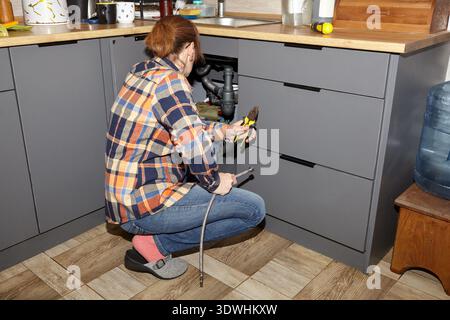 Woman fixing a plumbing issue  - sink pipe water leak. Cleaning out the clogged drain, trying to fix siphone in kitchen sink Stock Photo