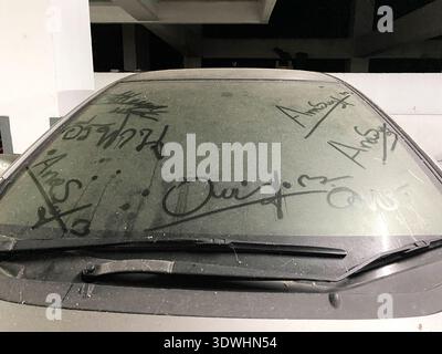 Dirty windshield of a parked car shows dust and markings, set in a dimly lit garage with concrete walls and shadows creating a moody atmosphere Stock Photo