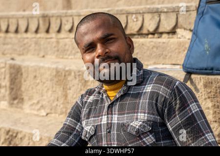 Close-up portrait of a painter artist sitting on stone steps in Varanasi, India, wearing a plaid shirt and yellow sweater. Stock Photo