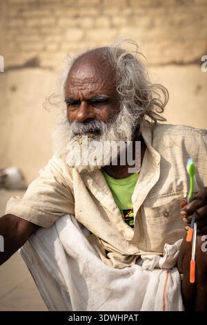 Portrait of an elderly man with a white beard holding toothbrushes in Varanasi, India, showcasing local life and culture. Stock Photo