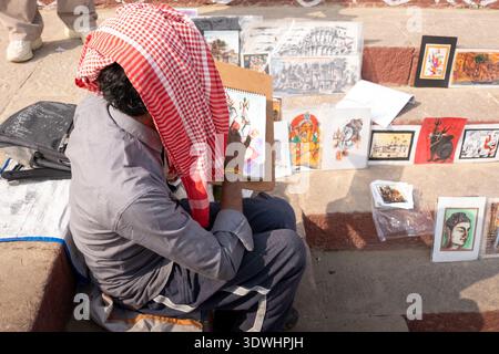 Artist painting Hindu religious artwork on the streets of Varanasi, India, surrounded by various colorful paintings. Stock Photo