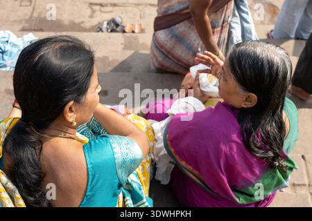 Two Indian women wearing colorful sarees sit on stone steps in Varanasi, India, enjoying a moment together. Stock Photo