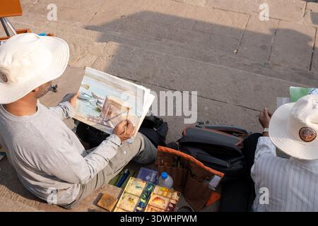 Two Indian painters in Varanasi working on watercolor paintings outdoors by stone steps. Stock Photo