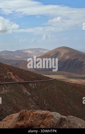 A road leads through the gentle brown mountains of Fuerteventura under a cloudy sky Stock Photo