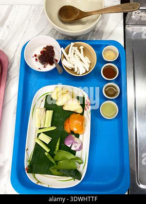 Ingredients for Thai Tom Yum soup are arranged on a blue tray, including herbs, spices, and vegetables, ready for cooking preparation Stock Photo