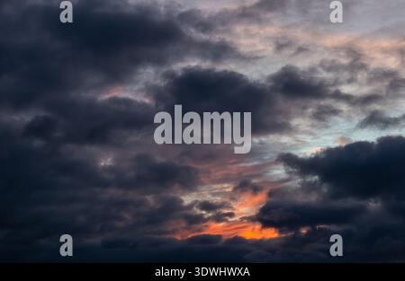Dark, heavy clouds gather across the sky with a small pocket of intense orange light breaking through at the bottom Stock Photo