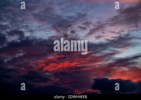 Vivid pink and orange light illuminates the undersides of dark clouds during a dramatic sunset Stock Photo