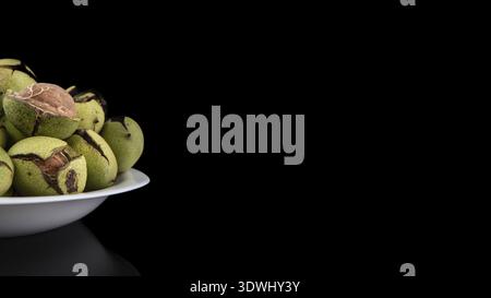 Green walnuts in the plate on a black background, cracked peel, fresh kernel Stock Photo