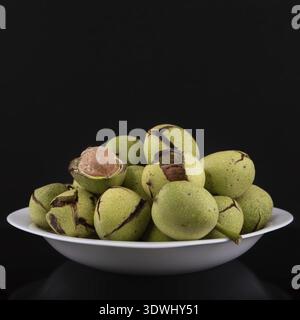 Green walnuts in the plate on a black background, cracked peel Stock Photo