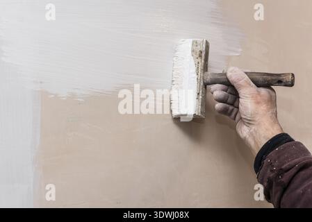 Master prime a putty wall before applying a decorative layer of plaster. Work process close-up. Interior repairs work Stock Photo