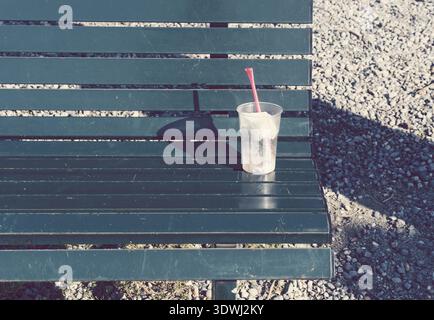 Disposable plastic drinks cup with straw lying on bench Stock Photo