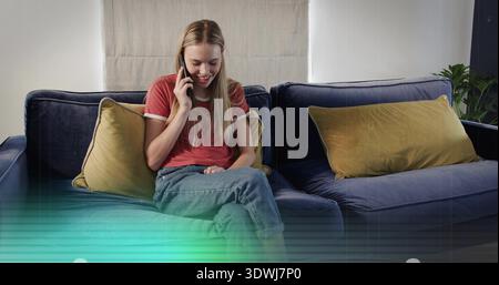 Smiling woman talking on smartphone while sitting on navy sofa in living room, wearing red T-shirt Stock Photo