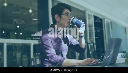 Analyzing data, Asian man typing on laptop in glass office, wearing plum shirt, sipping travel cup Stock Photo