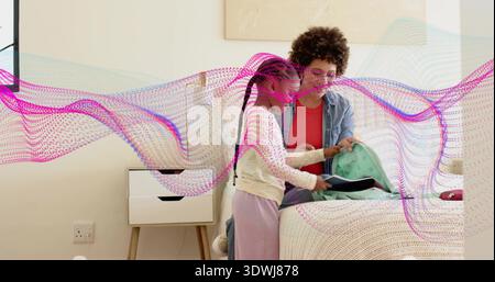 Helping mom in denim guiding girl placing notebook into mint-green backpack in bedroom, glasses Stock Photo