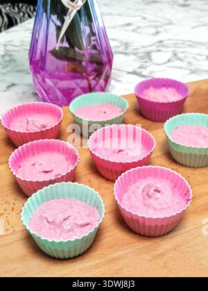 Pink and purple dough is laid out in silicone molds of pastel shades - blue, pink and purple. berry cake, neatly laid out on a wooden board, purple va Stock Photo