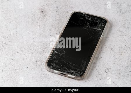 Modern mobile phone with broken screen on stone background. Cracked glass on smartphone closeup in focus Stock Photo