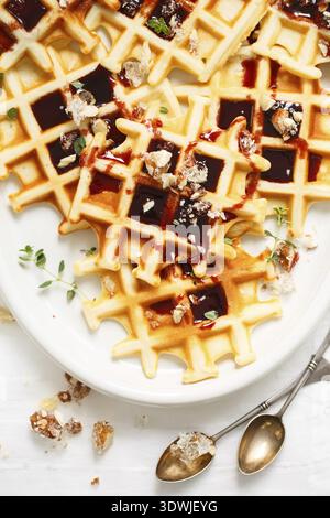 Belgian or Brussels waffles with date syrup or jam and candied roasted nuts. Homemade waffles in a white oval Plate on the kitchen table. Traditional Stock Photo
