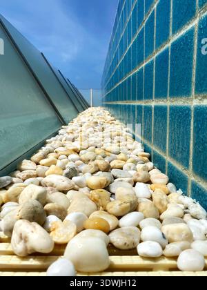 Decorative gravel pathway lined with smooth pebbles alongside a blue tiled wall, featuring a clear sky and modern architectural elements in a pool Stock Photo