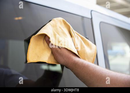 Man wipes car to shine using yellow microfiber. Process after car washing, close up view. Self-service in outdoors car wash Stock Photo