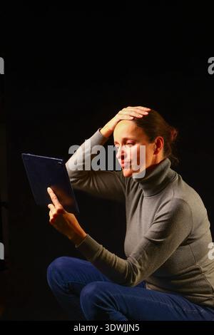 Woman sitting with a tablet in a moment of deep focus, symbolizing modern technology, independent work, digital literacy and the confident role of wom Stock Photo