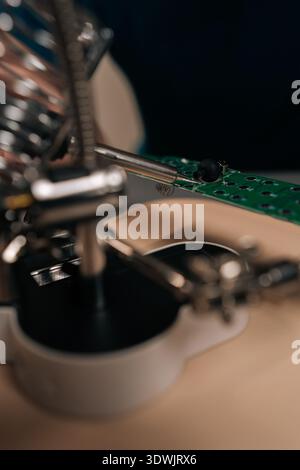 Vertical cropped shot of technician using soldering iron and magnifier to repair an electronic circuit board, focusing on precision engineering Stock Photo