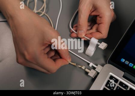 Person hands inspecting frayed and exposed laptop power cord, highlighting wear and tear, product damage, and the need for electronic repair or Stock Photo