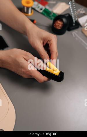 Vertical cropped shot of person preparing wires with a stripping tool for electronic circuit assembly on a workbench, engaging in a diy project or Stock Photo