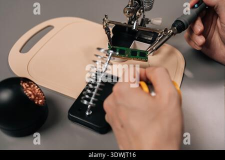Close-up hand of technician soldering computer ram module using a helping hands tool and a soldering iron, repairing electronic components on a Stock Photo