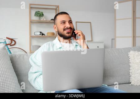 Young man working with laptop while talking on mobile phone Stock Photo
