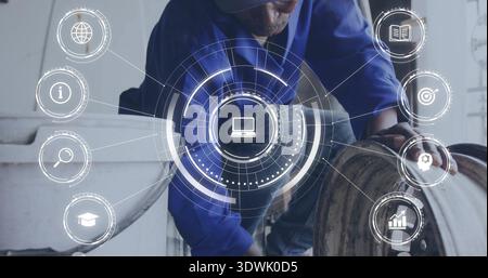 Crouching tech in blue shirt and cap inspecting drum, white tank at workshop, with HUD overlay Stock Photo