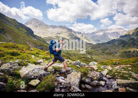 Man hiker with backpack crossing mountain stream during hiking tour in European Alps, Styria, Austria. Outdoors adventure on trekking trail Stock Photo