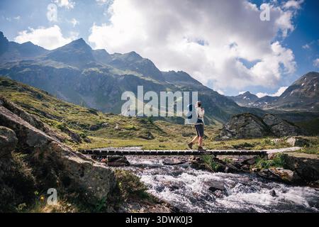 Backpacker crossing wooden bridge over mountain stream on hiking trail in Austrian Alps mountains. Solo hike adventure Stock Photo