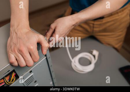 Close-up of technician connecting a power cable to the back of a desktop computer, ensuring proper power supply installation for system setup and Stock Photo