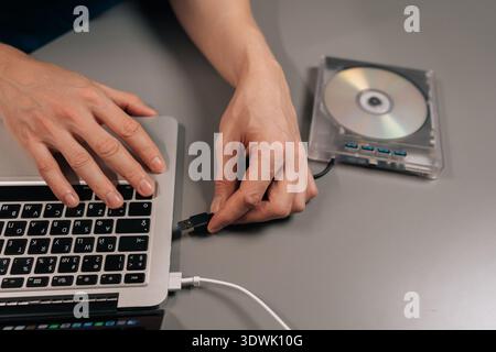 Person connecting a portable optical disk reader to a modern notebook computer via usb, enabling access to cd and dvd content or installing systems on Stock Photo
