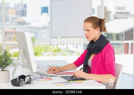 Female in pink cardigan using stylus on graphics tablet near monitor at office, copy space. Designer, creativity, urban, cityscape, daylight, minimali Stock Photo